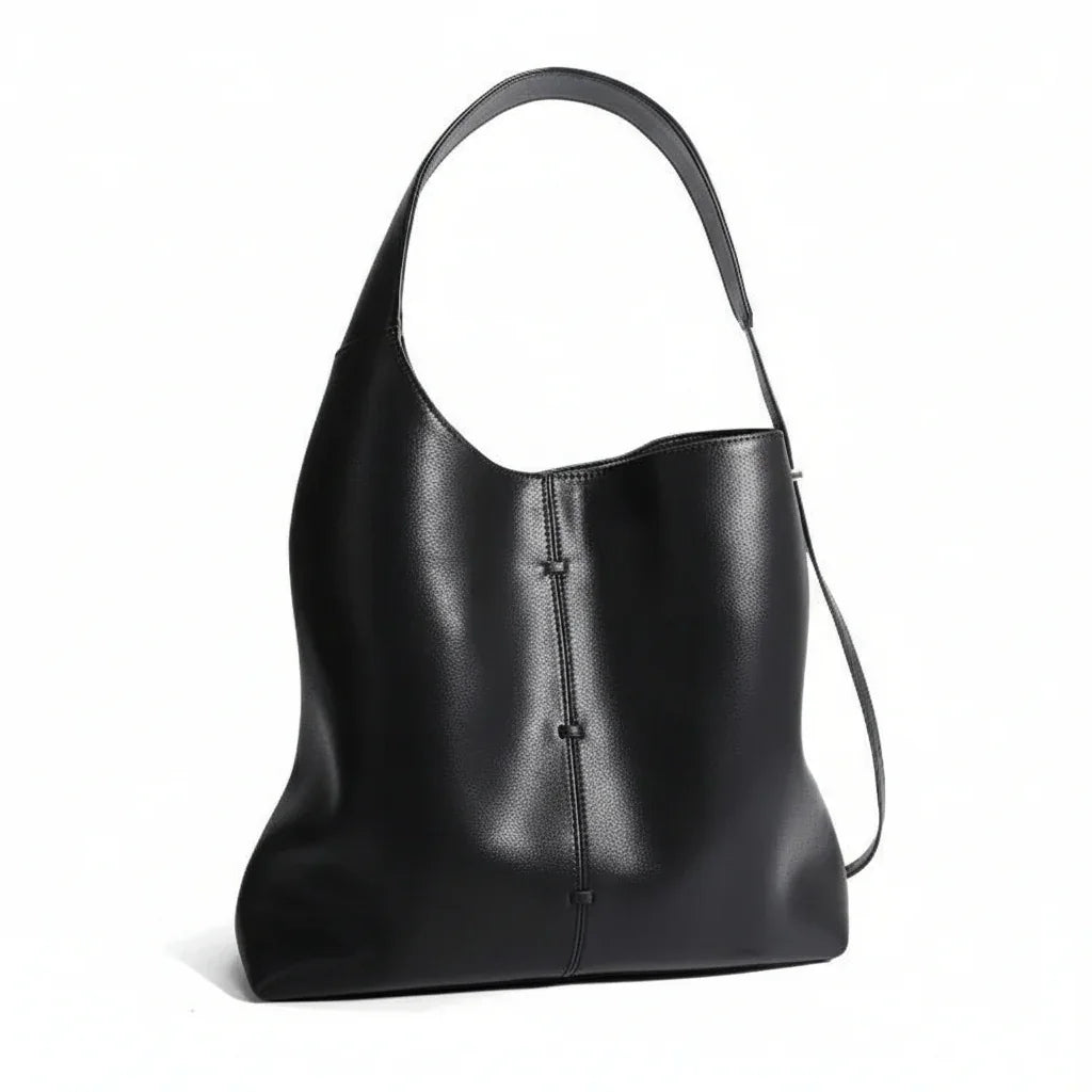Black leather shoulder bag with single strap and minimalist stitch detail on white background