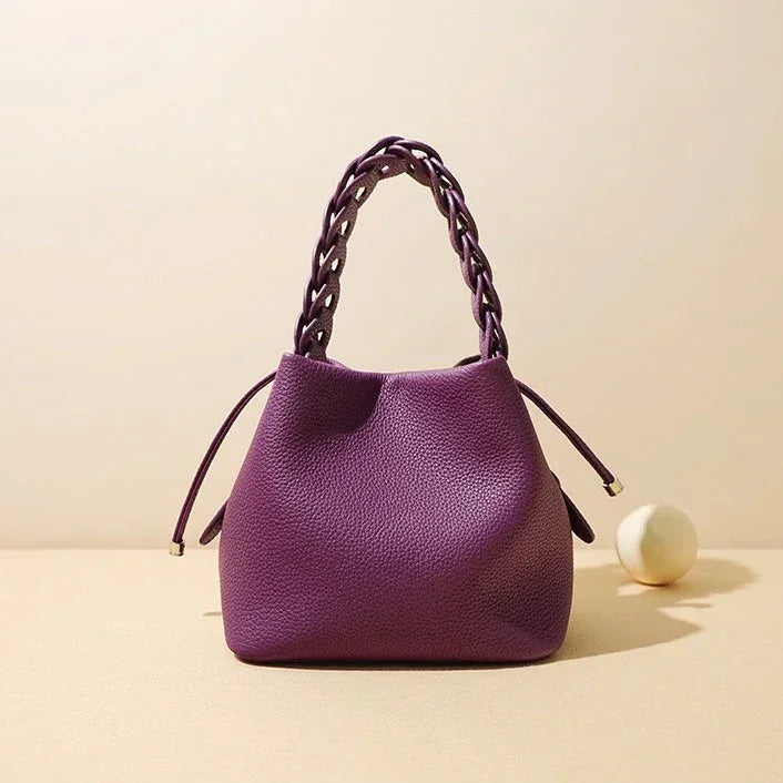 Purple textured handbag with braided handle on beige background