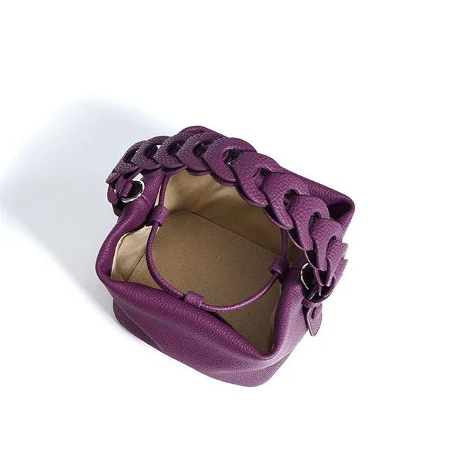 Purple leather handbag with chunky braided handle and beige interior on white background