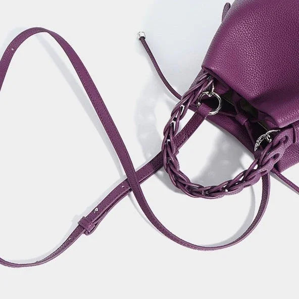 Purple leather crossbody bag with braided handle on white background