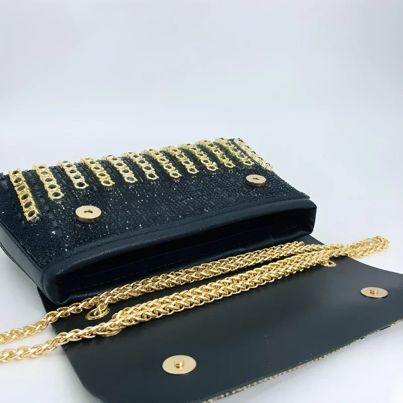 Black sequin clutch purse with gold chain strap and grommet accents on white background