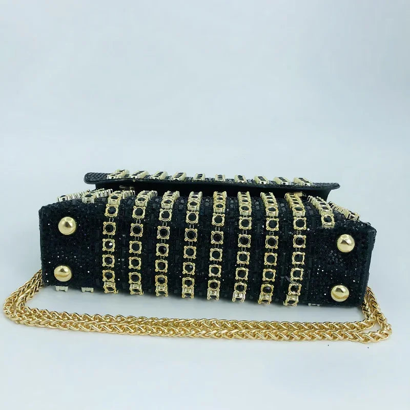 Black handbag with gold studs, chain strap, and geometric metal accents on a white background