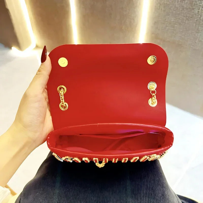 Hand holding open red purse with gold chain and button closure, modern indoor setting