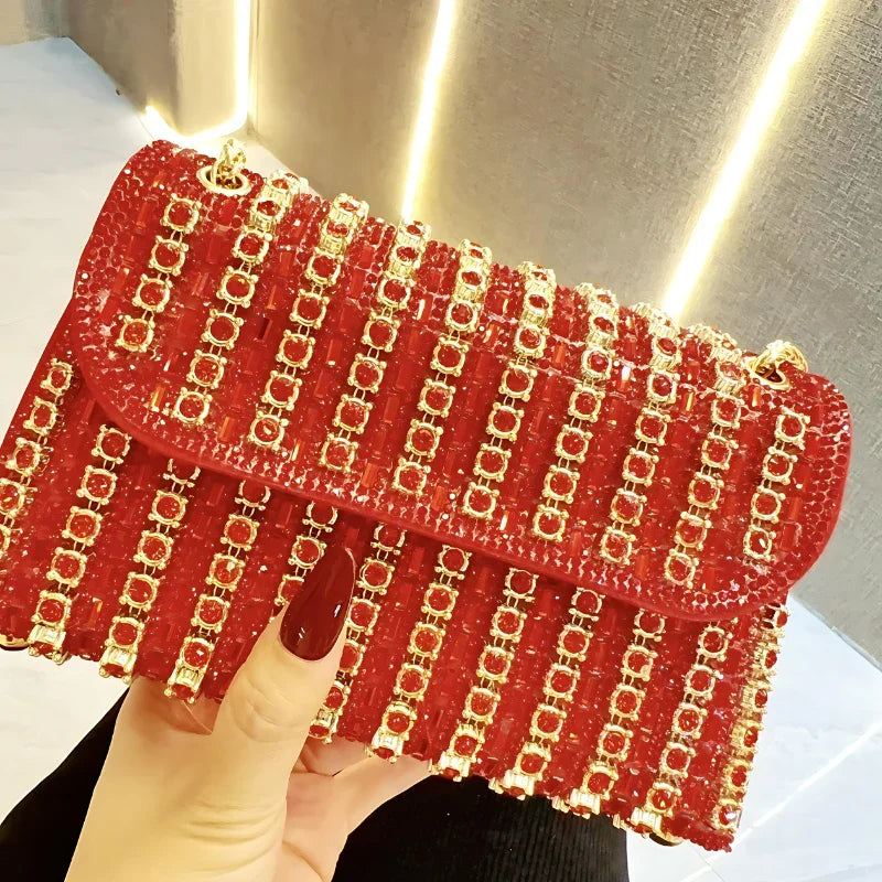 Red beaded clutch bag with gold chain embellishments, held by a hand with red nails