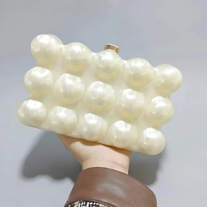 Hand holding a pearl bubble clutch bag with textured, glossy spheres against a plain background