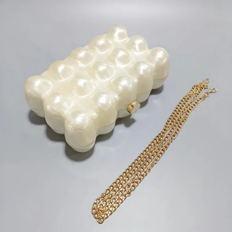 Pearl pattern clutch bag with gold chain strap on a gray surface
