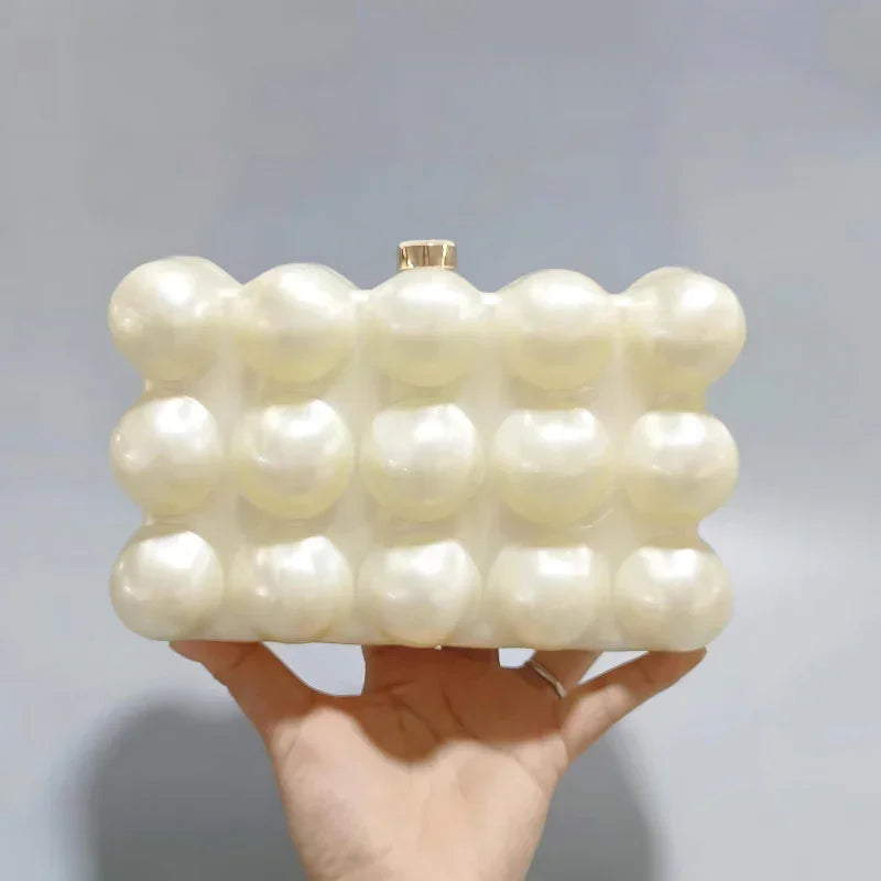 Hand holding a pearl bubble texture clutch purse against a plain background
