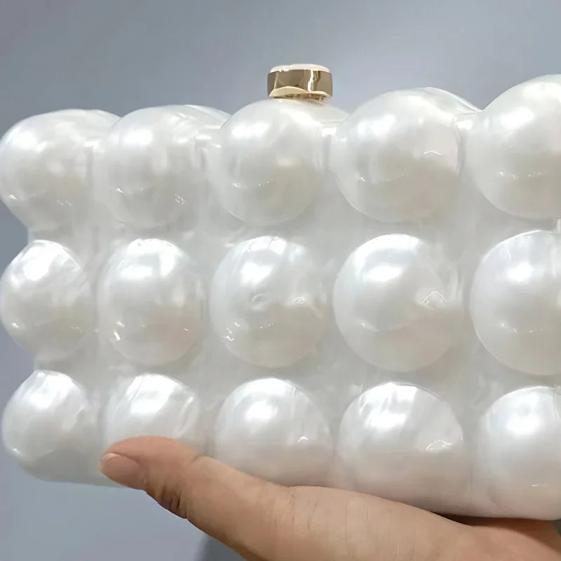 Hand holding pearl bubble clutch bag with gold clasp against neutral background
