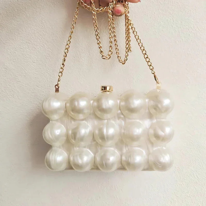 Pearl beaded clutch purse with gold chain strap held against a light background