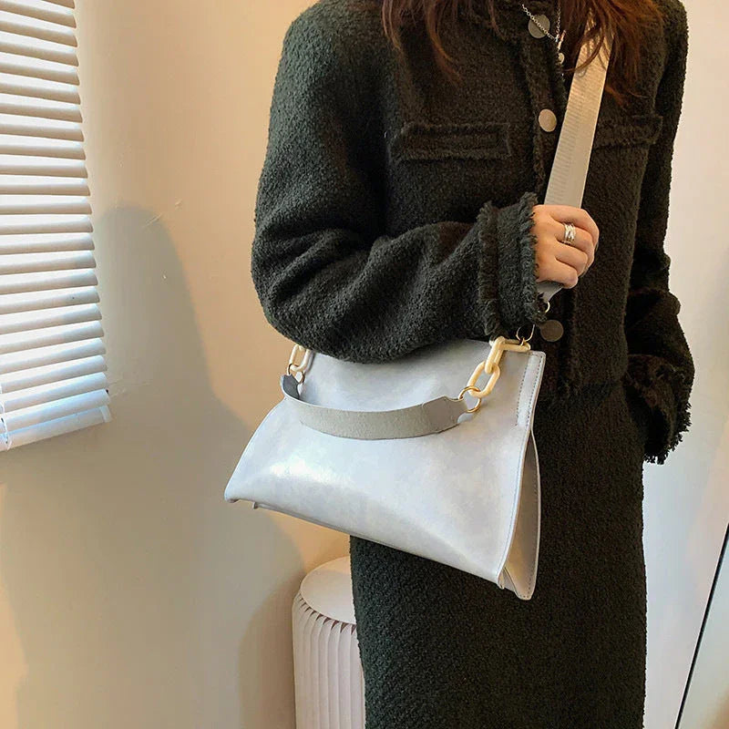Woman wearing a dark textured coat holding a stylish light gray shoulder bag indoors