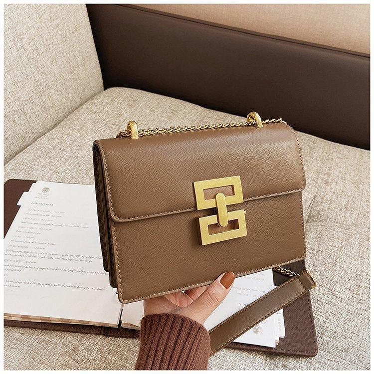 Brown leather shoulder bag with gold chain and geometric clasp on beige sofa