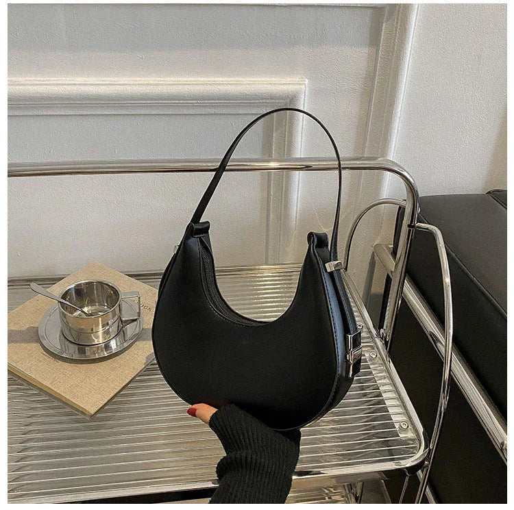 Black crescent shoulder bag on metal rack, modern minimalist interior, coffee cup nearby