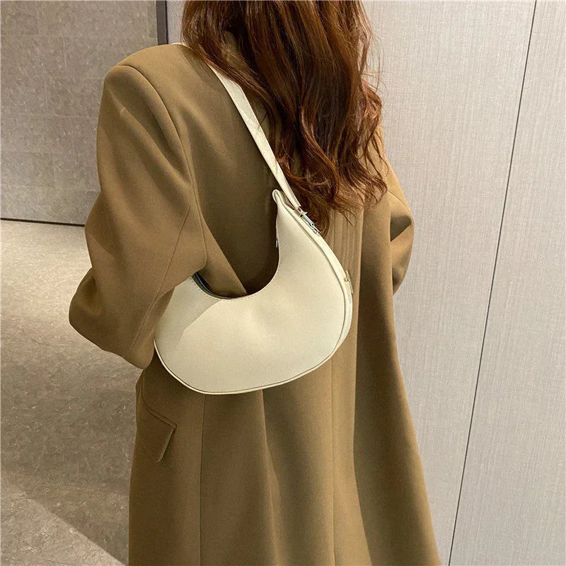 Woman in brown coat carrying white crescent shoulder bag, modern minimalist style