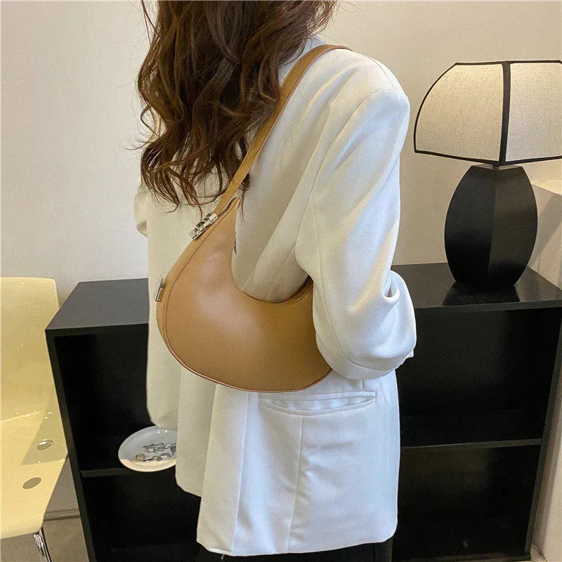 Woman wearing a white blazer and tan shoulder bag in a modern room with a black lamp