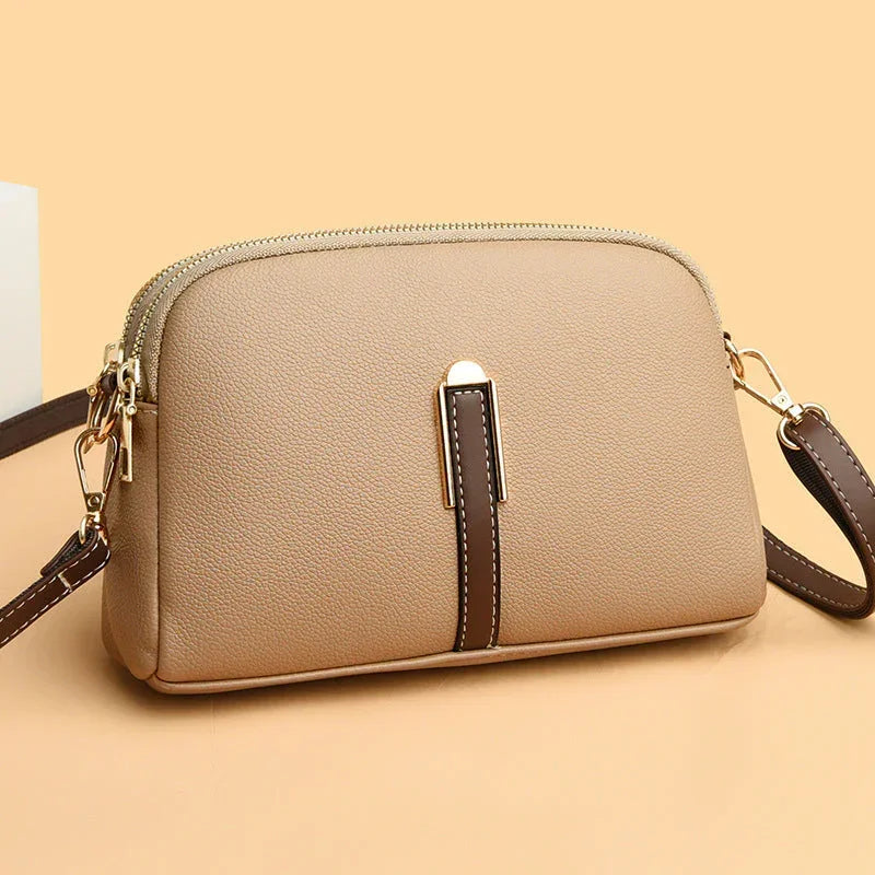 Beige crossbody leather bag with zipper and dark brown accent on a light background