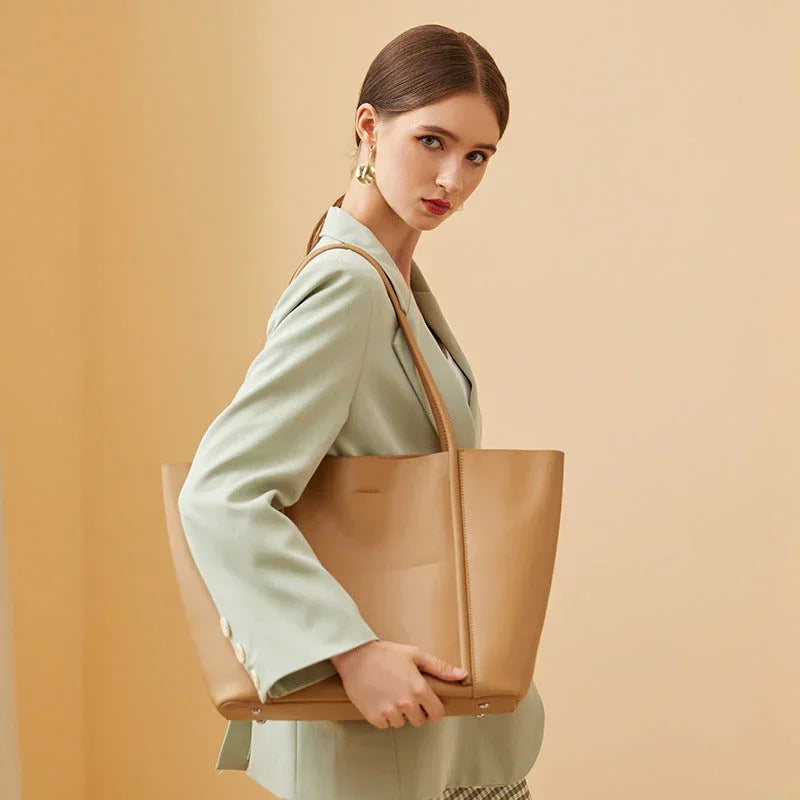 Woman in light green blazer holding large tan leather tote bag on beige background