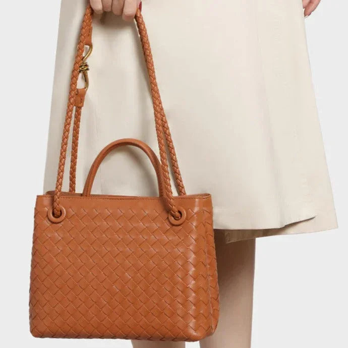Woman holding a brown woven leather handbag with braided shoulder straps, cream dress