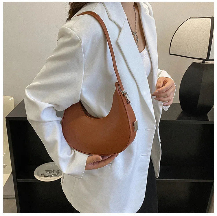Woman in white blazer holding brown crescent shoulder bag in modern interior