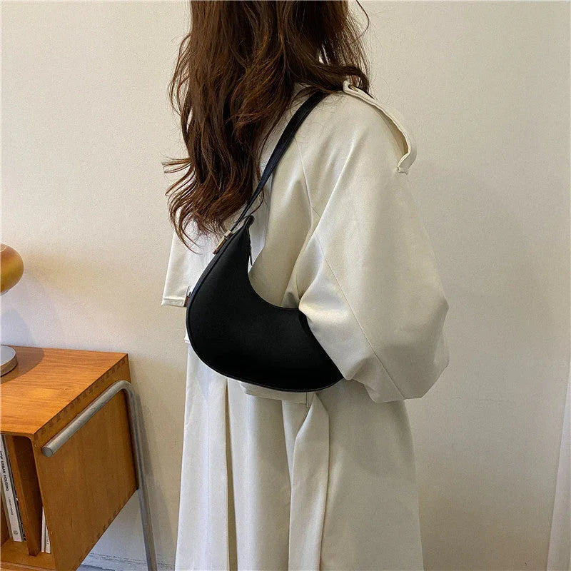 Woman in cream coat with black shoulder bag stands by wooden desk