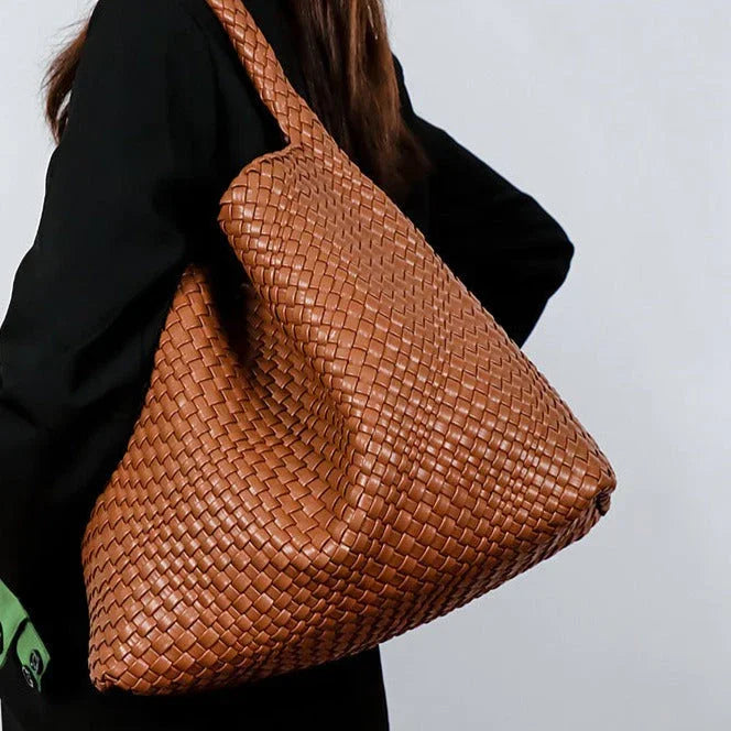 Woman carrying large woven brown leather tote bag over shoulder