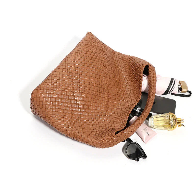 Brown woven tote bag with sunglasses, perfume, umbrella, and cosmetics on white background