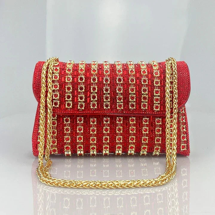 Red clutch purse with gold studs and gold chain strap on a gray background