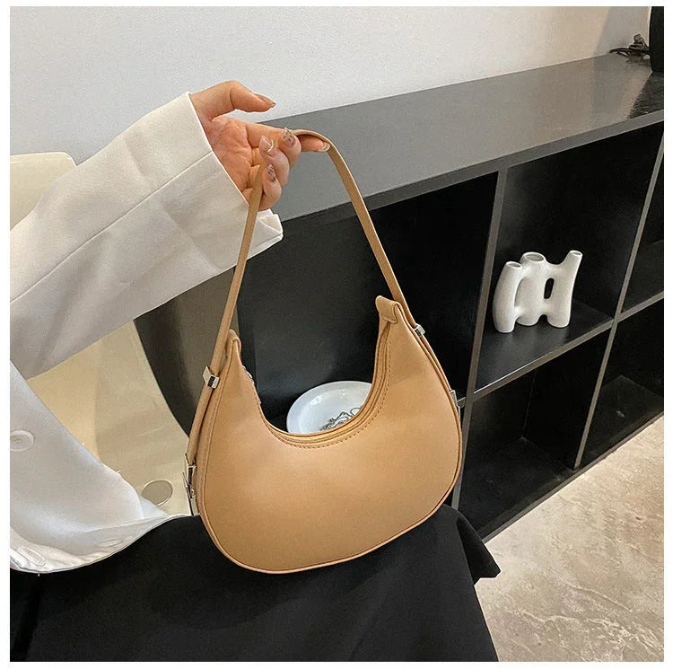 Woman holding beige crescent shoulder bag in modern minimalist room with black shelving