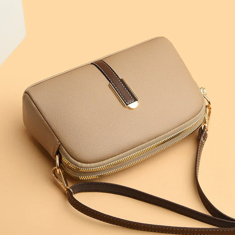 Beige leather crossbody bag with gold zipper and brown strap on a tan background