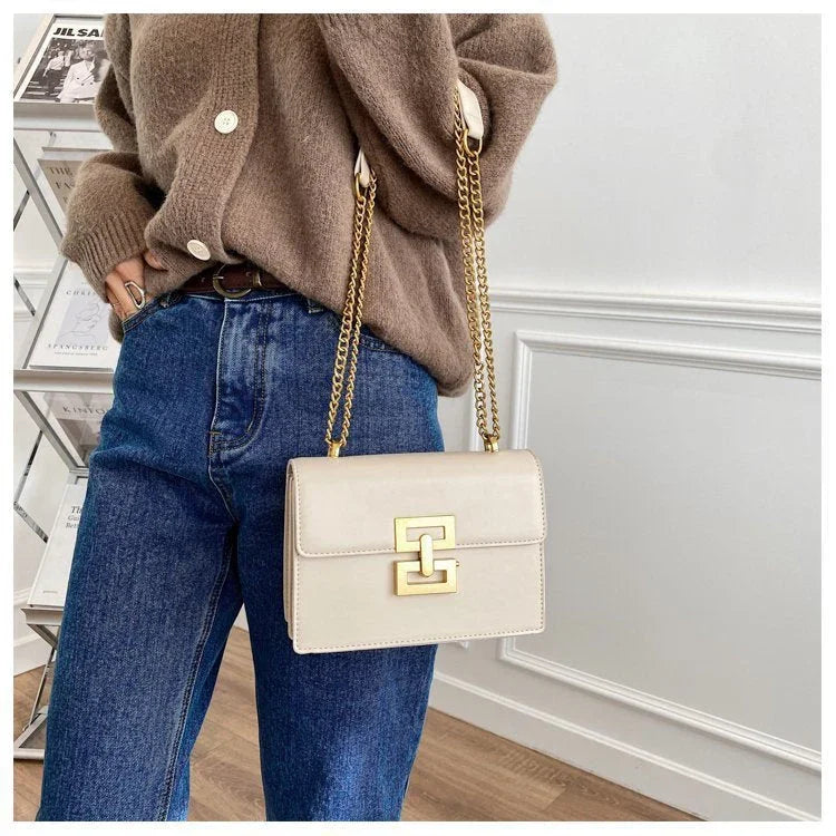 Woman in brown sweater and jeans holding beige chain strap shoulder bag with gold buckle