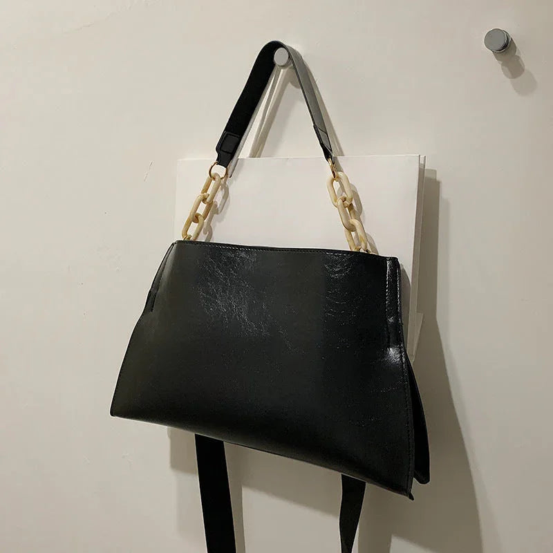 Black leather handbag with beige chain strap hanging on a wall hook