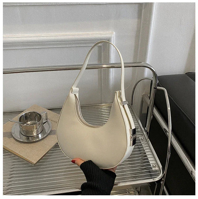 White crescent shoulder bag on metal shelf, minimalist modern purse with handle