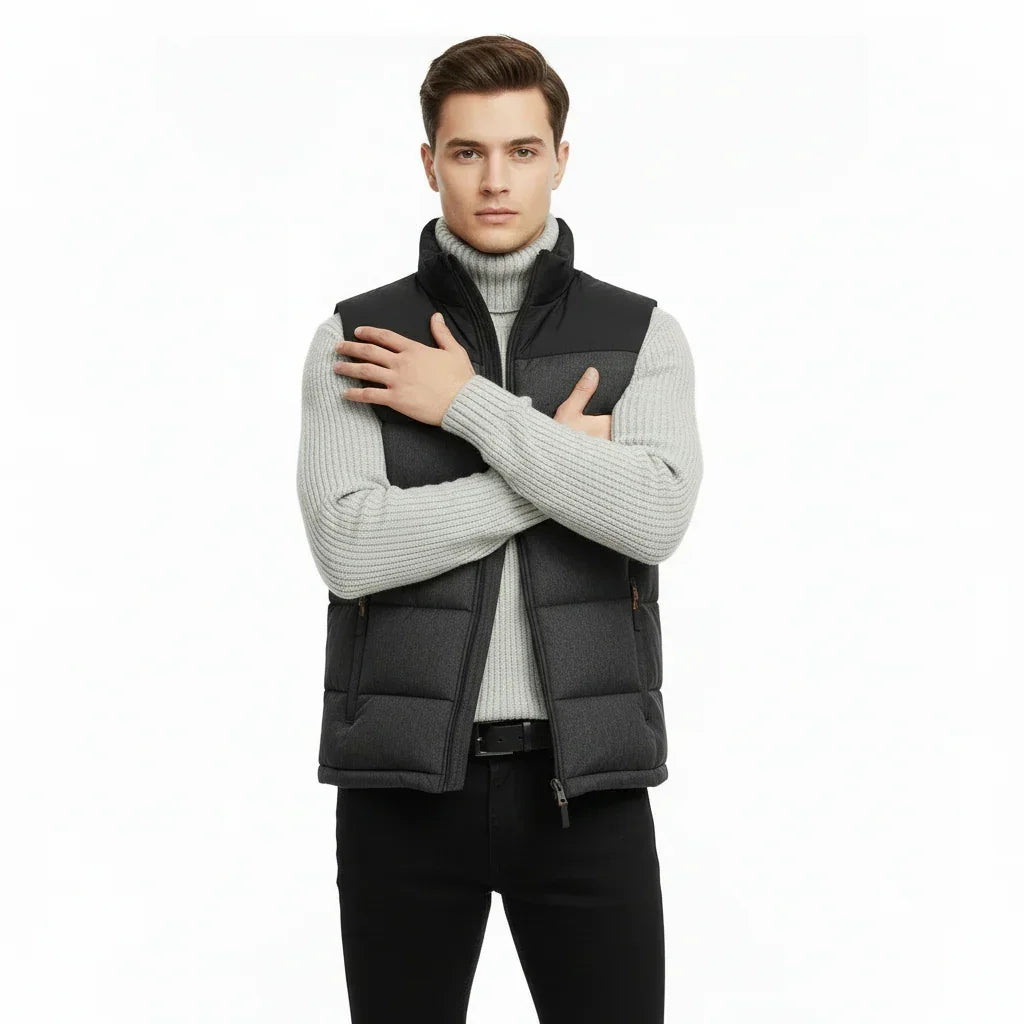 Man wearing a black puffer vest over a gray sweater on a white background