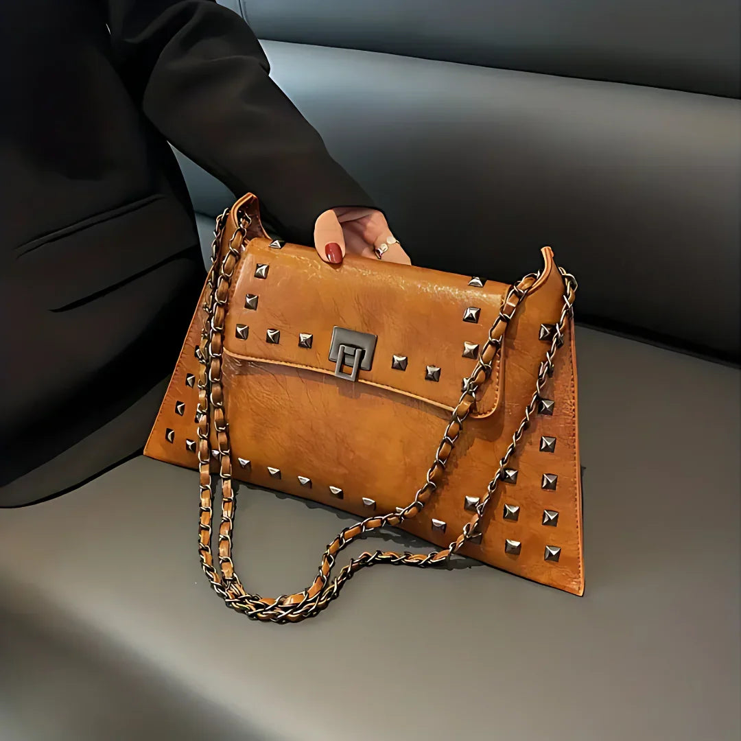 Brown leather studded handbag with chain strap on gray sofa