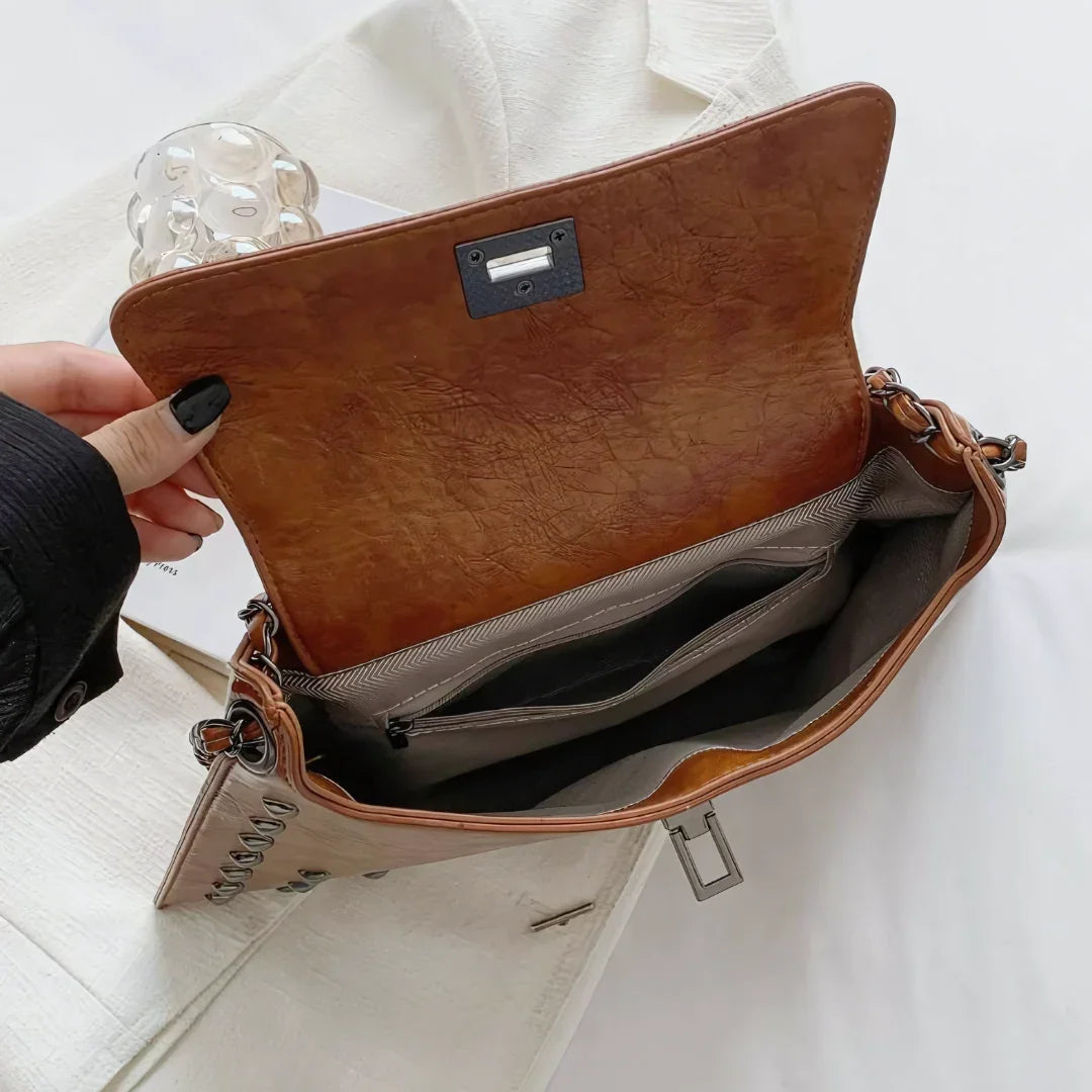 Brown leather shoulder bag open to show spacious interior and multiple pockets on white fabric