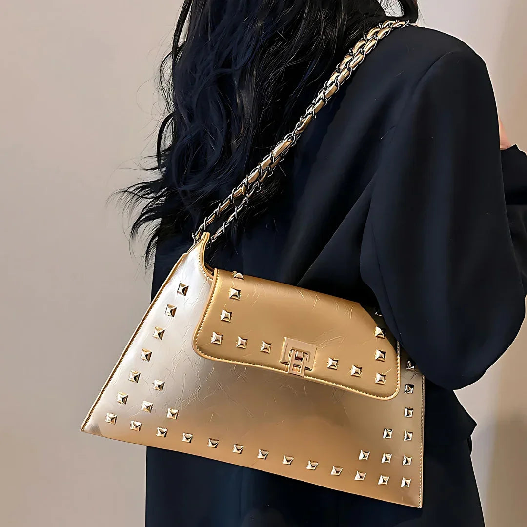 Gold studded handbag with chain strap worn over black outfit, luxury fashion accessory