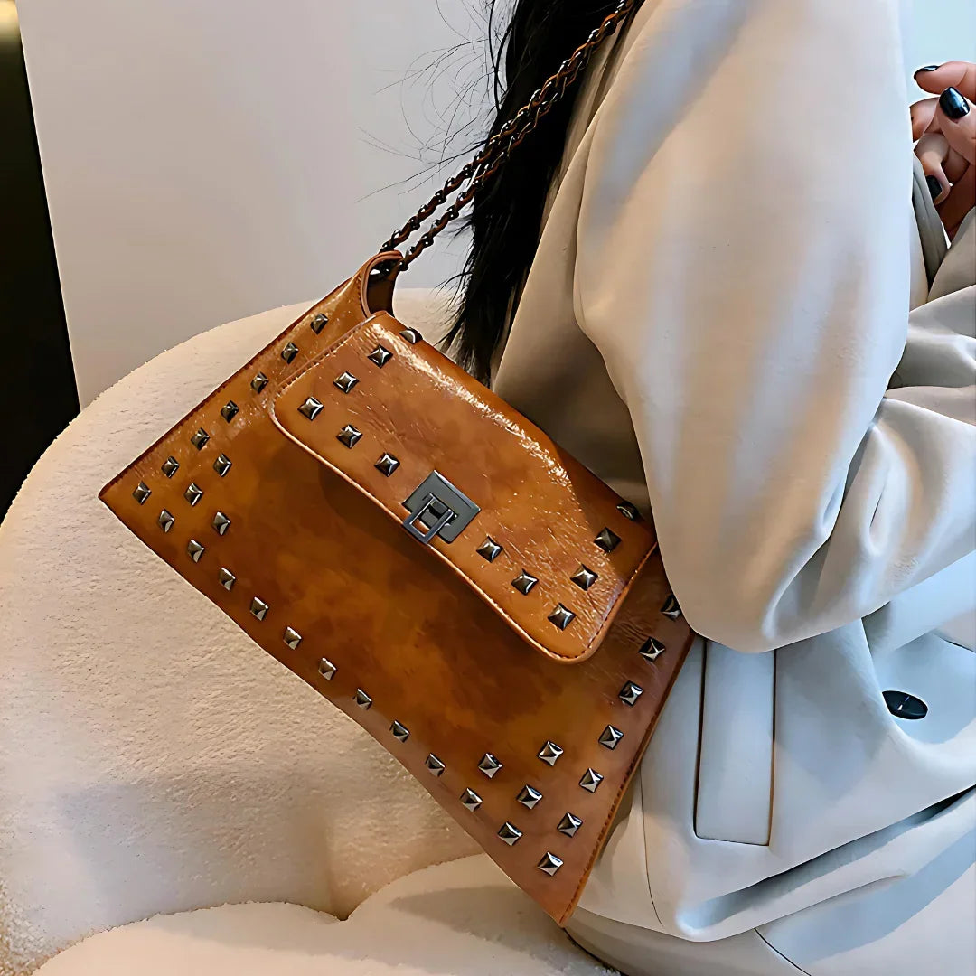 Brown leather studded shoulder bag with chain strap, worn over a light beige blazer