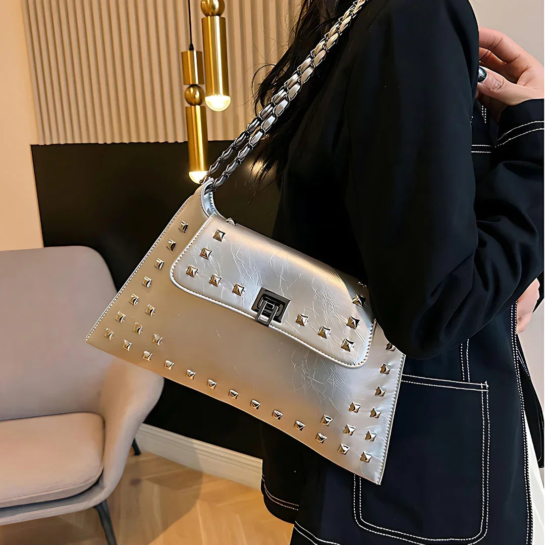 Silver studded shoulder bag with chain strap, worn by woman in black blazer indoors