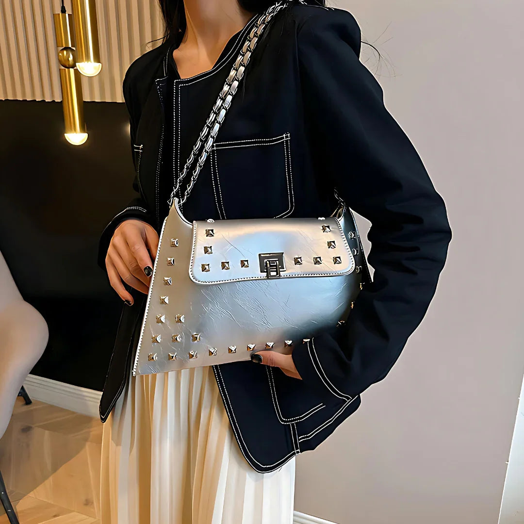 Woman in black blazer holding silver studded handbag with chain strap indoors