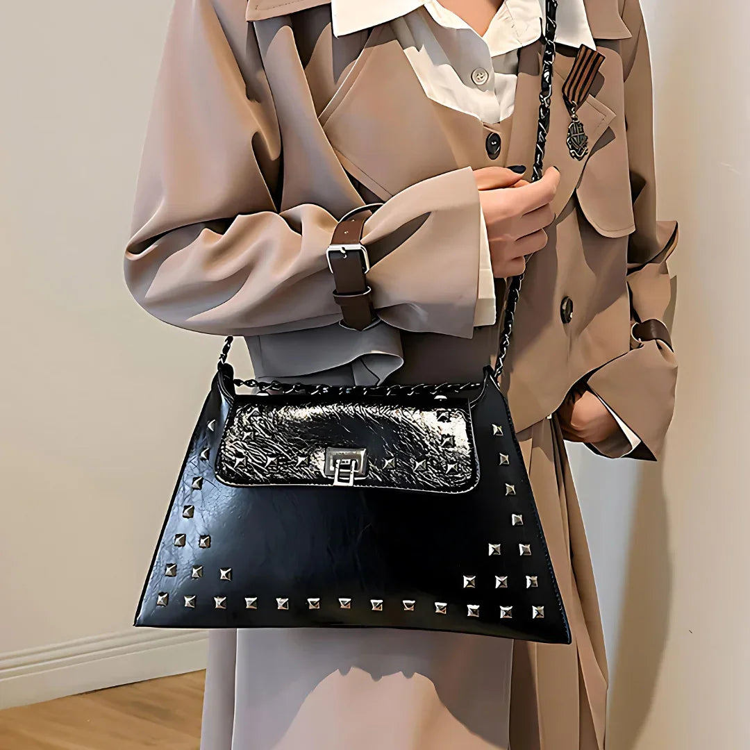 Woman in beige trench coat holding a black studded leather handbag with chain strap