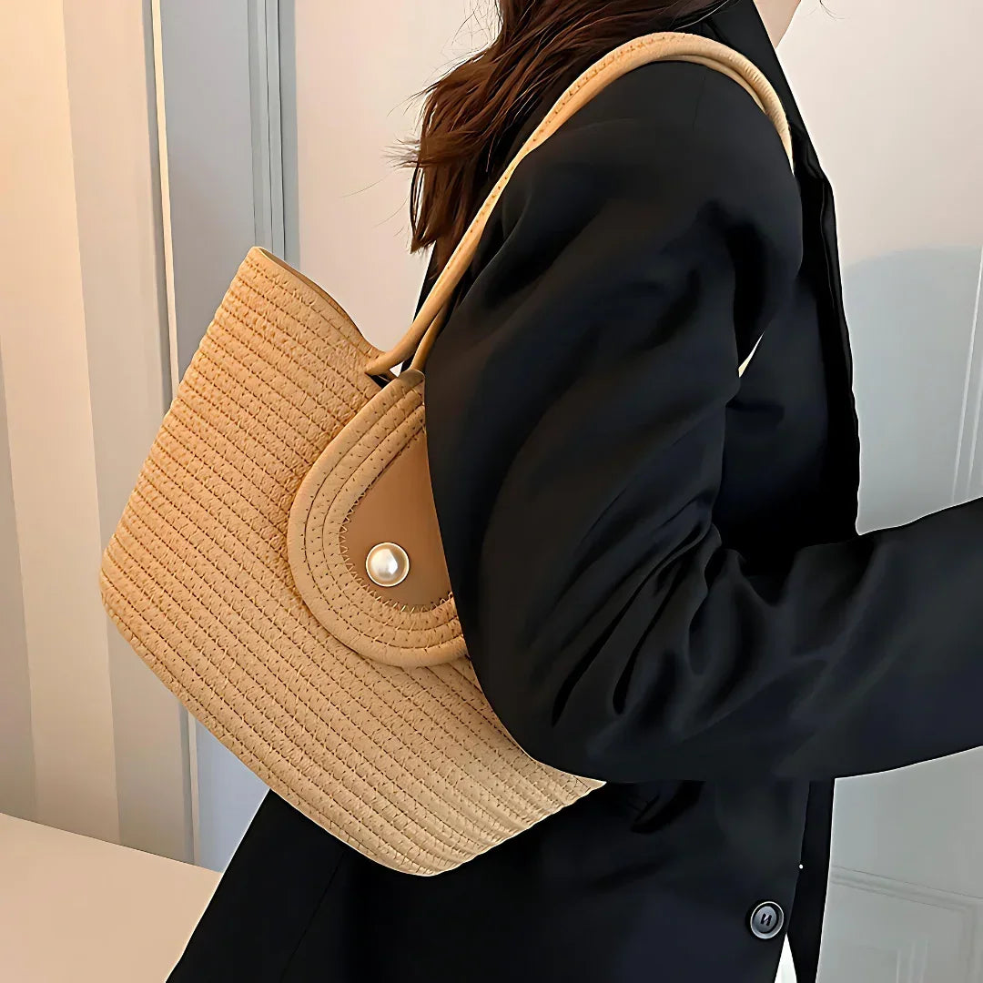 Woman in black blazer carrying a beige woven straw shoulder bag indoors