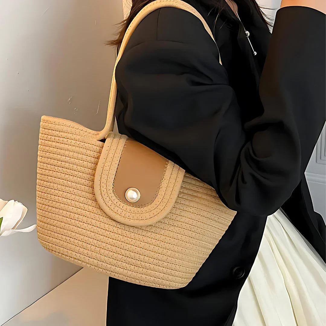 Woman carrying beige woven shoulder bag with pearl button, black blazer, and cream skirt