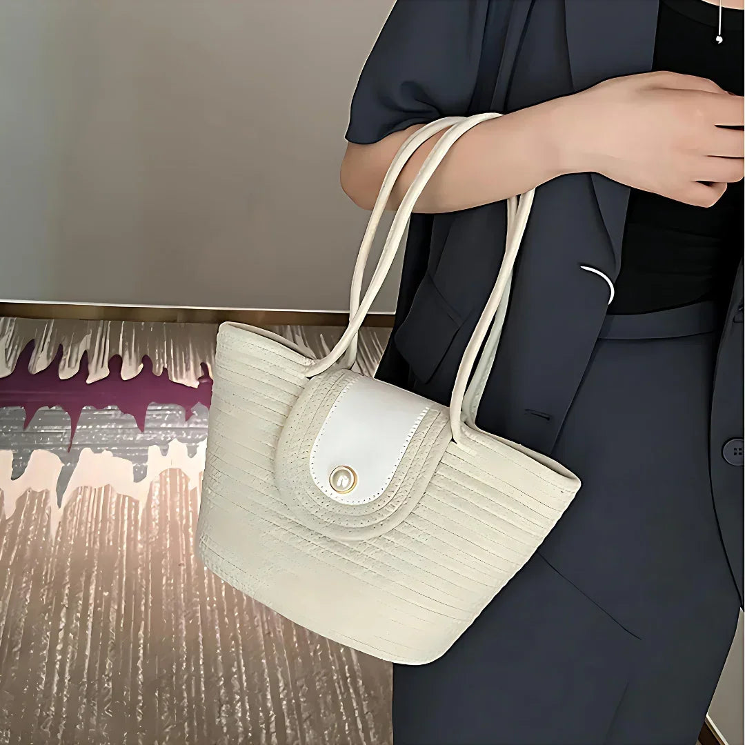 Woman holding cream quilted tote bag with gold clasp, dressed in navy suit indoors