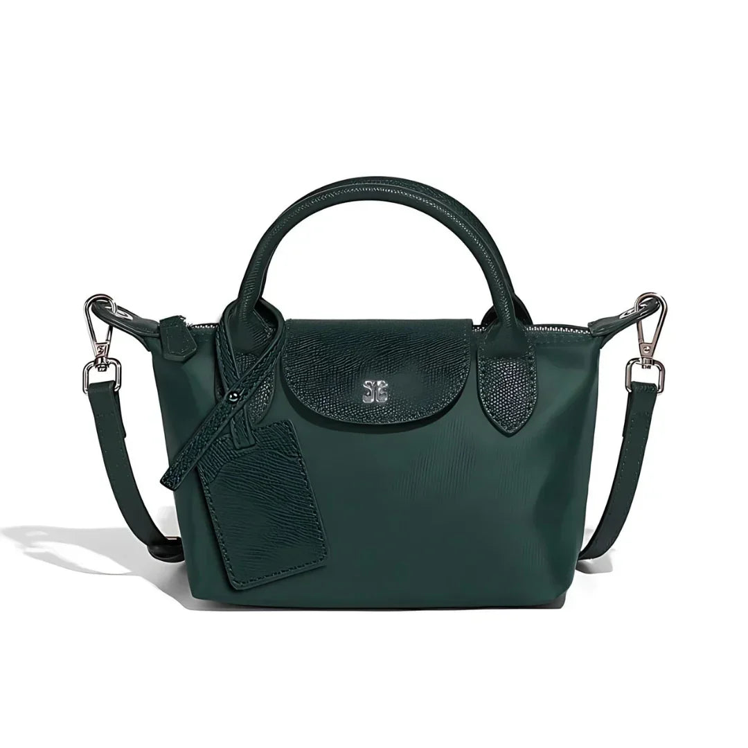 Dark green leather handbag with top handles, shoulder strap, and luggage tag on white background