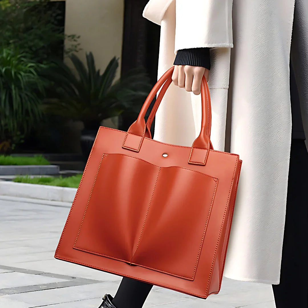 Woman in white coat holding large orange leather tote bag outdoors