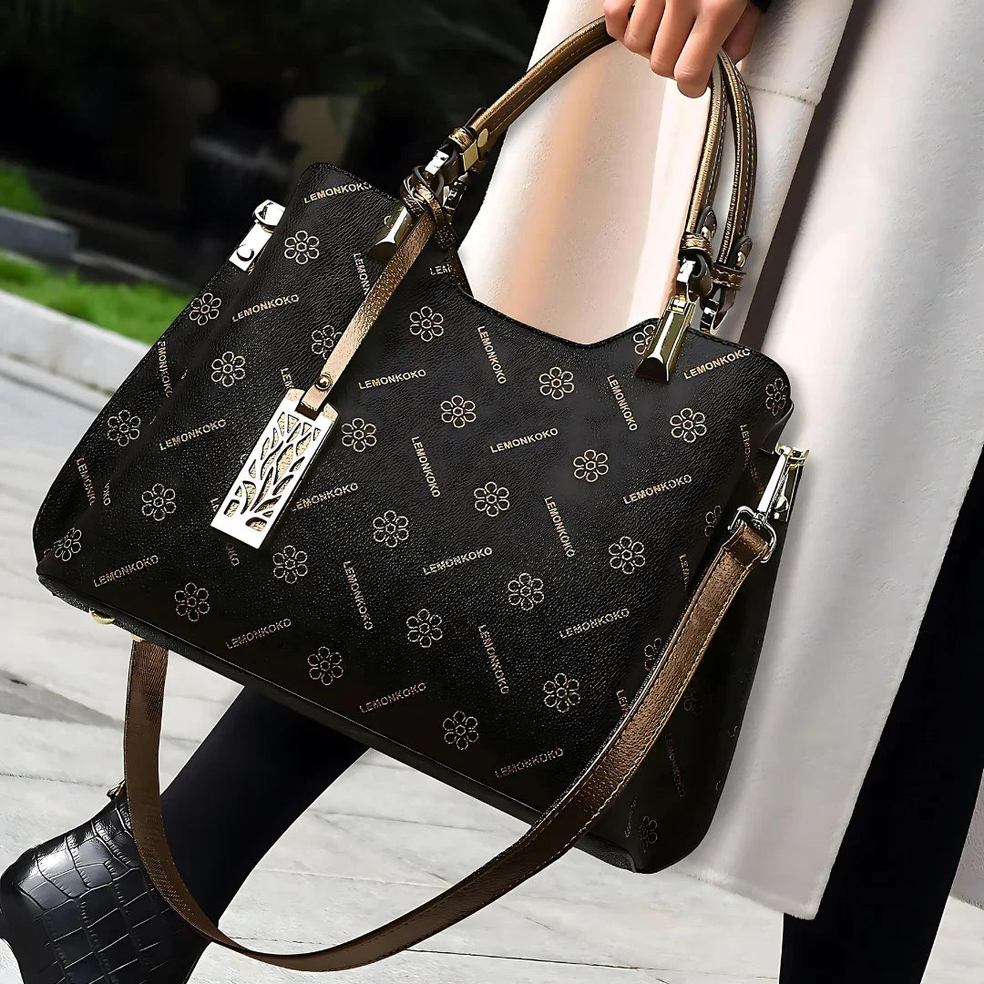 Woman carrying black LEMONKOKO handbag with gold floral print and double handles