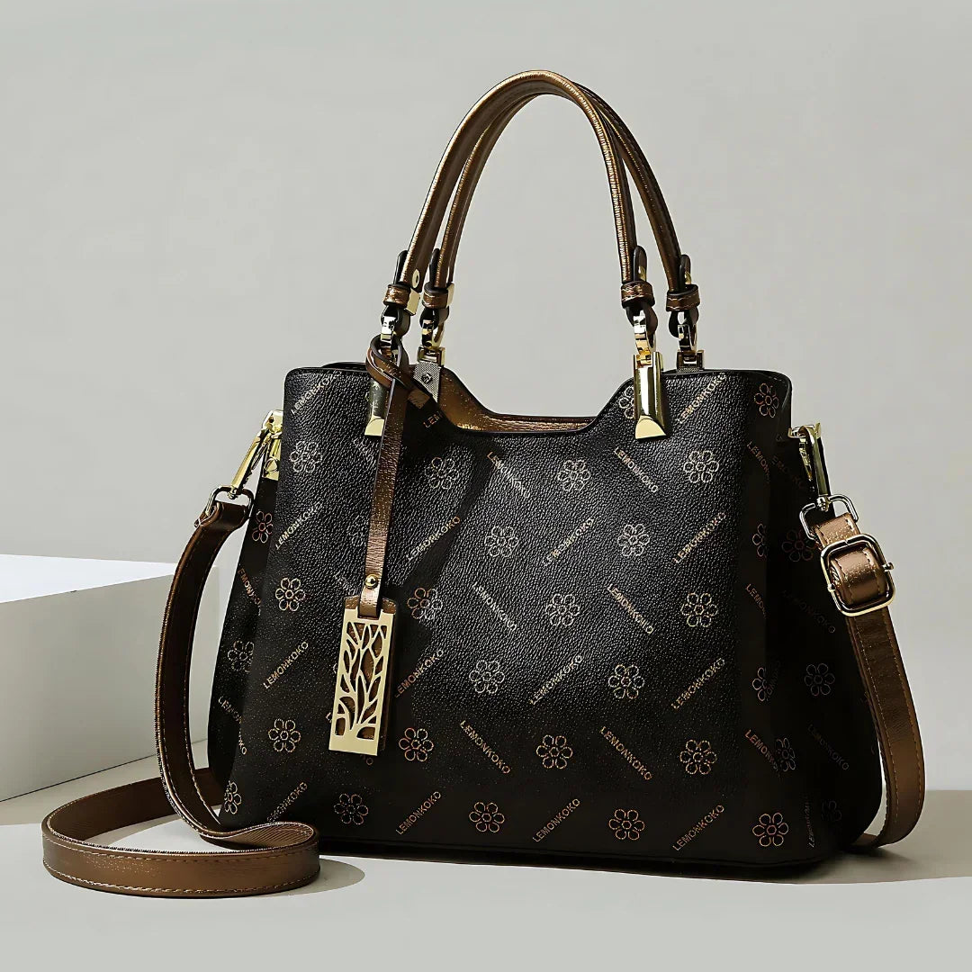 Elegant black and brown leather handbag with floral pattern and gold hardware on neutral background.