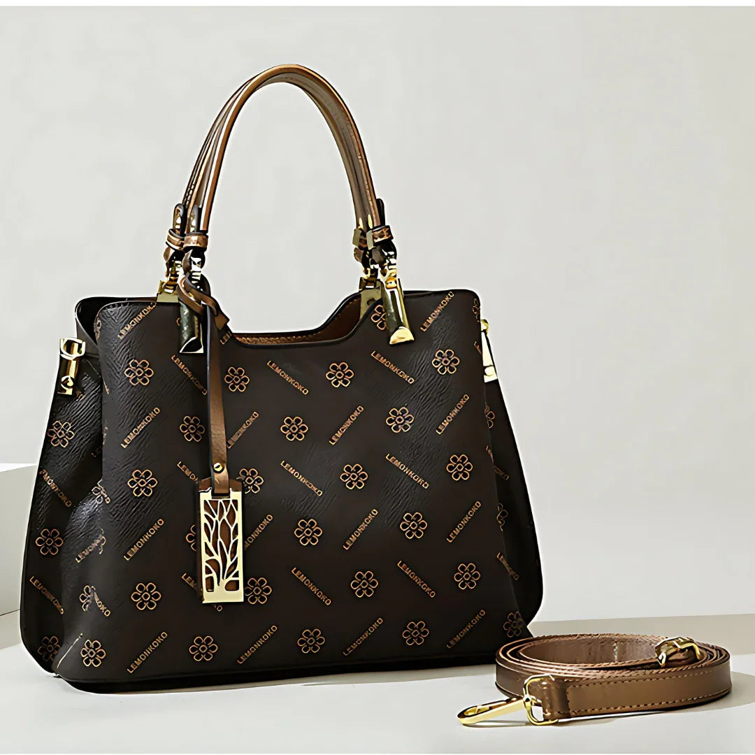 Brown designer handbag with floral pattern, gold hardware, and detachable strap on table