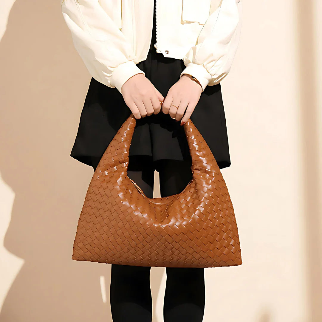Woman holding a large woven brown leather hobo bag, wearing black skirt and cream jacket