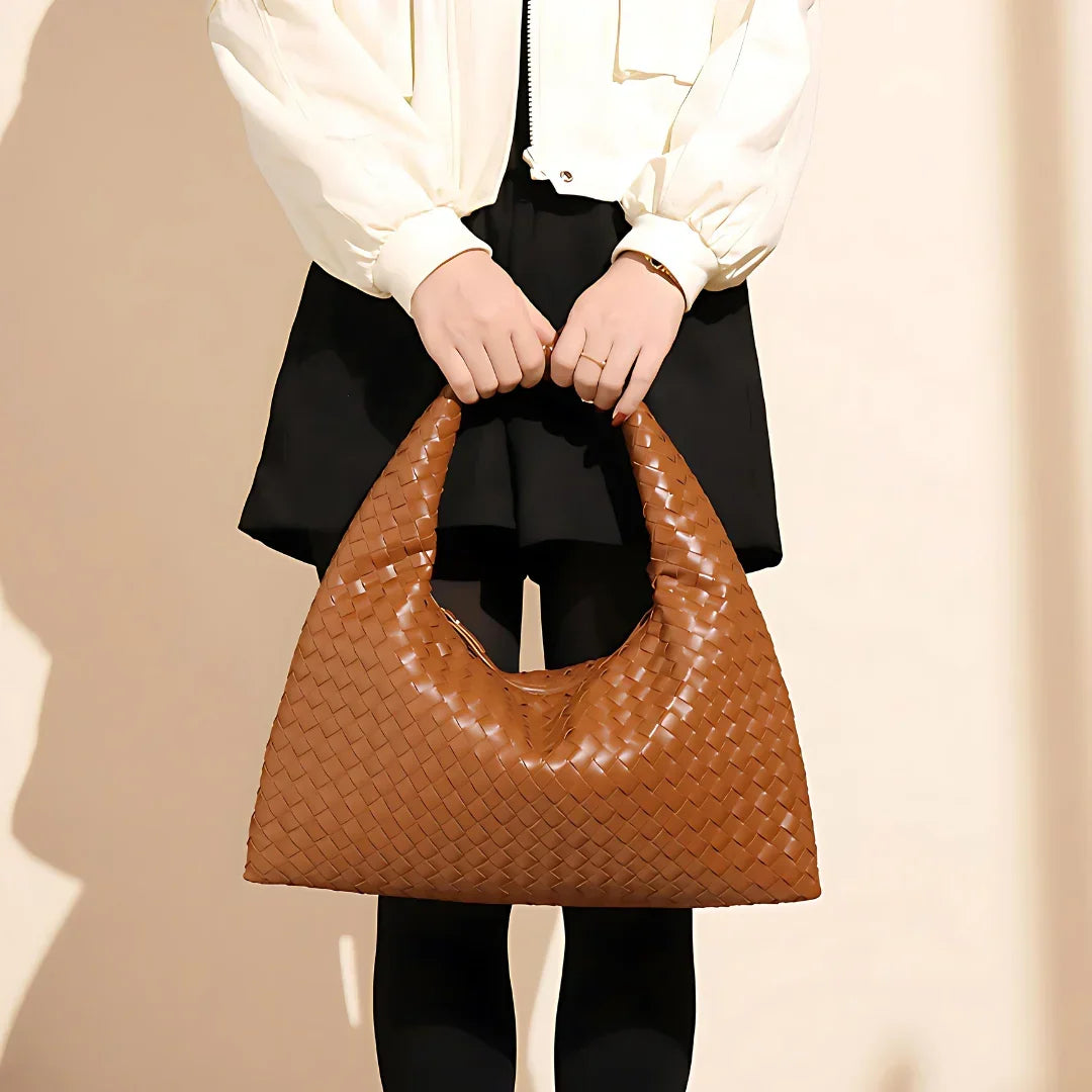 Woman holding a large woven brown leather hobo bag, wearing black skirt and cream jacket