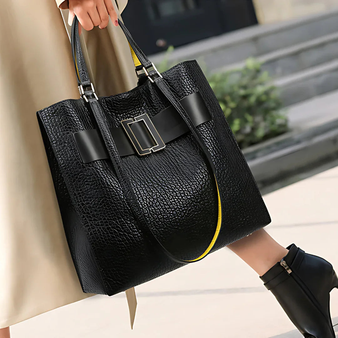 Woman carrying large black textured leather tote bag with buckle detail on city sidewalk
